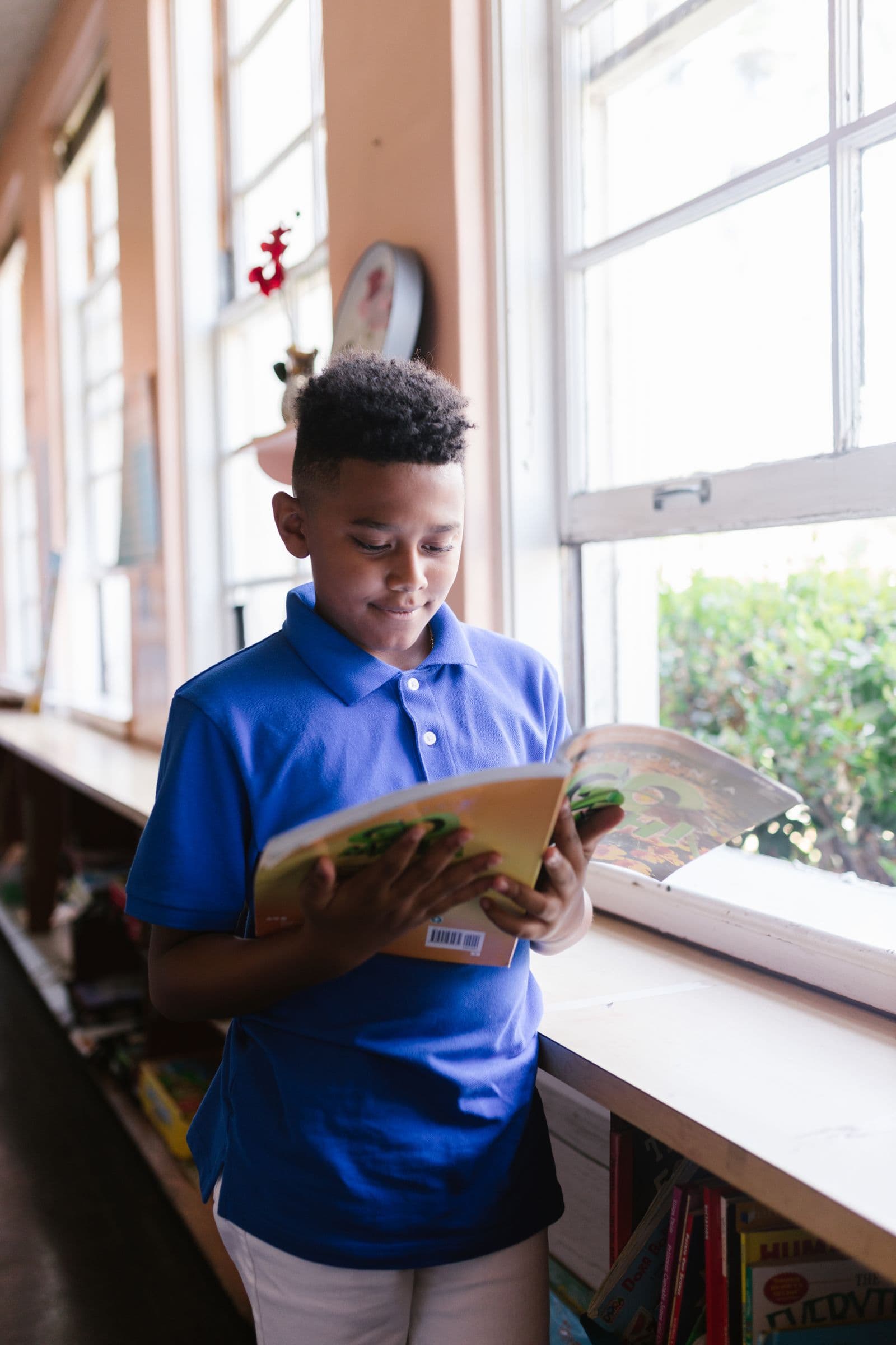 African schoolboy reading a textbook by the classroom window